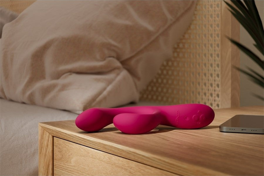 Nova Rabbit Vibrator placed on a wooden nightstand next to a bed, showing its sleek, compact design